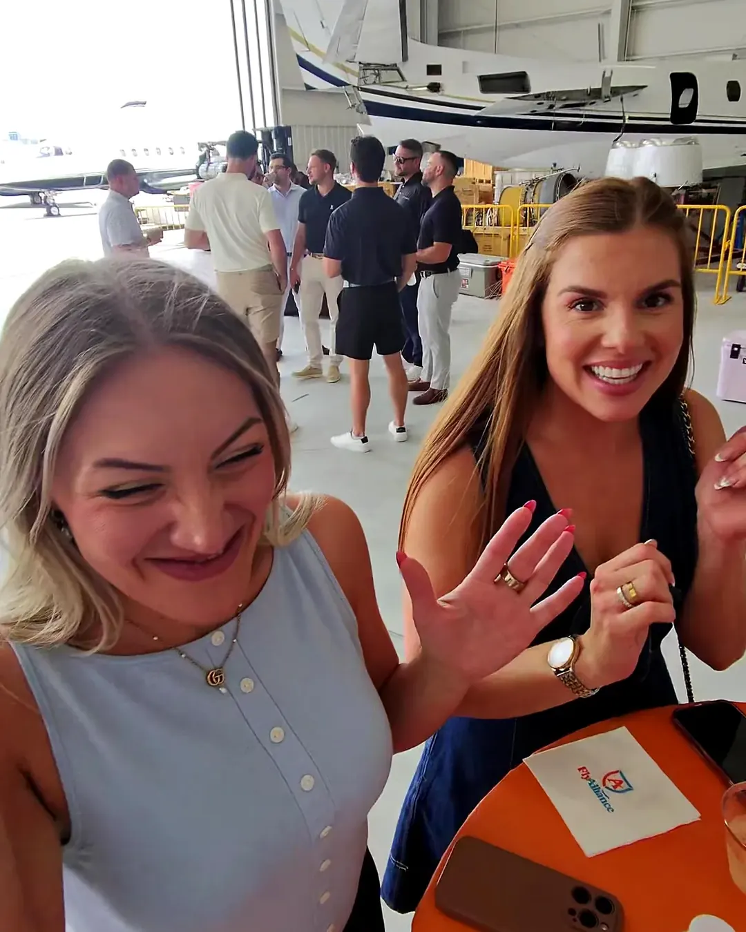 Two guests laughing together at a corporate party in a jet hangar